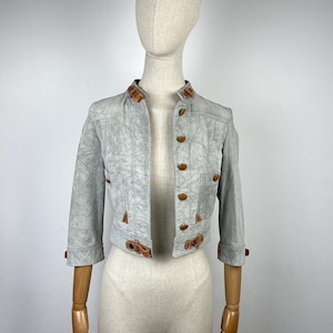 May include: A light gray cropped leather jacket with brown leather trim and buttons. The jacket has a stand-up collar and long sleeves.