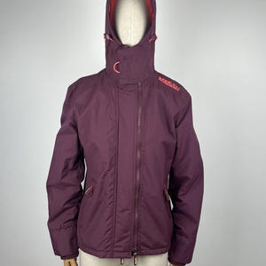 Peut inclure: Une veste à capuche bordeaux avec une fermeture éclair et un logo Superdry rose sur la manche droite.