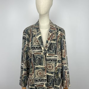 Puede incluir: Un blazer estampado en tonos beige, marrón, verde y negro. El blazer presenta un diseño geométrico con solapas de muesca, dos bolsillos delanteros y mangas largas. La prenda se exhibe en un maniquí.