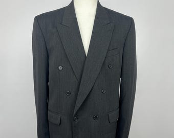 Könnte beinhalten: Ein anthrazitfarbener, zweireihiger Blazer mit fallendem Revers. Der Blazer hat sechs schwarze Knöpfe, zwei Vordertaschen und eine taillierte Passform. Die Jacke wird auf einer Schaufensterpuppe präsentiert.