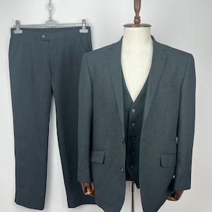 May include: A three-piece charcoal gray suit, including a blazer, vest, and trousers. The blazer and vest are displayed on a mannequin, while the trousers hang on a hanger. The suit is made of a solid, textured fabric.