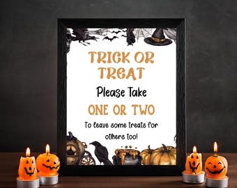 May include: A framed Halloween sign with the text "TRICK OR TREAT Please Take ONE OR TWO To leave some treats for others too!" surrounded by spooky illustrations. Two lit pumpkin candles sit in front of the frame.