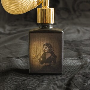 A black perfume bottle with a vintage ivory atomizer features artwork of a skeletal woman in Victorian dress holding a lantern, set against eerie script-like wallpaper. The moody shadows and muted gold glow conjure a ghostly presence, capturing the claustrophobic dread and uncanny beauty at the heart of the fragrance’s inspiration.