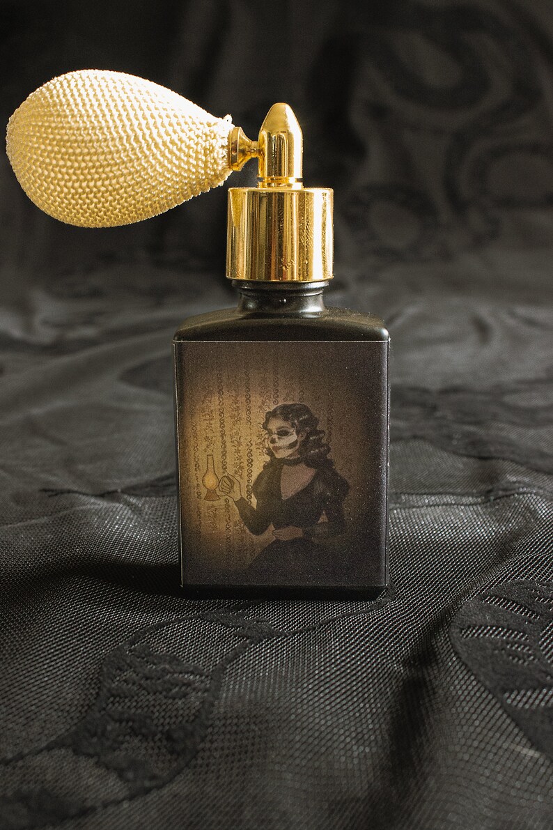 A black perfume bottle with a vintage ivory atomizer features artwork of a skeletal woman in Victorian dress holding a lantern, set against eerie script-like wallpaper. The moody shadows and muted gold glow conjure a ghostly presence, capturing the claustrophobic dread and uncanny beauty at the heart of the fragrance’s inspiration.