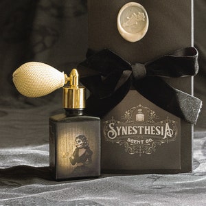 A gothic perfume bottle with an ivory atomizer and sepia-toned artwork of a skeletal woman holding a lantern stands before an ornate Synesthesia Scent Co. box sealed with a pale wax crest. The fabric backdrop and soft golden light create an atmosphere of haunted elegance, echoing the suffocating beauty and unsettling madness of its literary namesake.
