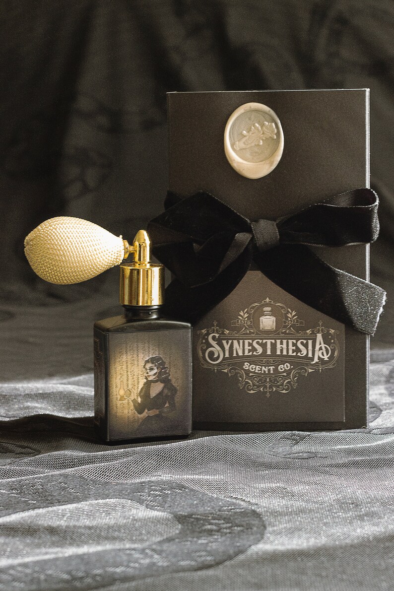 A gothic perfume bottle with an ivory atomizer and sepia-toned artwork of a skeletal woman holding a lantern stands before an ornate Synesthesia Scent Co. box sealed with a pale wax crest. The fabric backdrop and soft golden light create an atmosphere of haunted elegance, echoing the suffocating beauty and unsettling madness of its literary namesake.