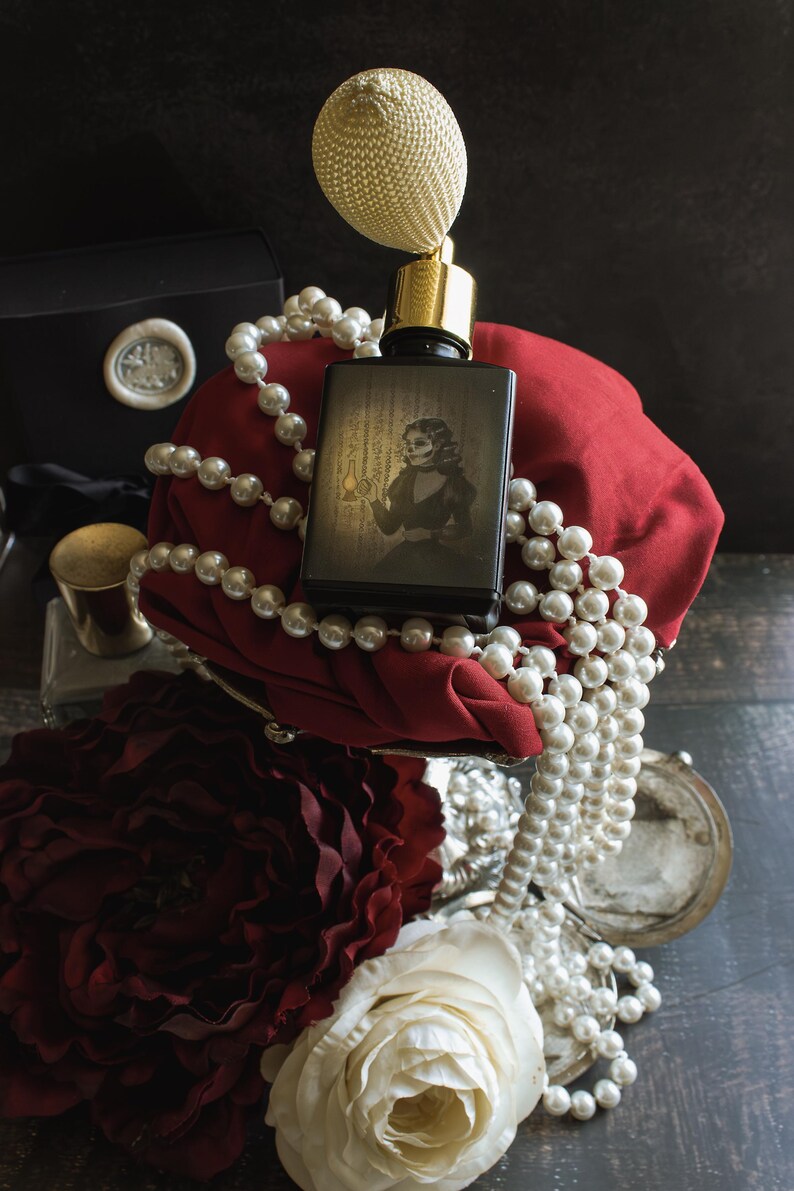 A bottle of “The Yellow Wallpaper” perfume with a golden atomizer rests against red fabric, draped in pearl strands, its illustrated label depicting a spectral woman holding a lantern. The dimly lit scene, framed by wilted roses and shadow, feels like a fever dream of beauty unraveling—where opulence curdles into claustrophobic dread.