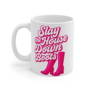 Op de afbeelding: Witte keramische mok met de tekst "Slay the House Down Boots" in roze letters. Het ontwerp bevat een paar roze laarzen met hoge hakken. De mok heeft een gebogen handvat en is geschikt voor warme of koude dranken.