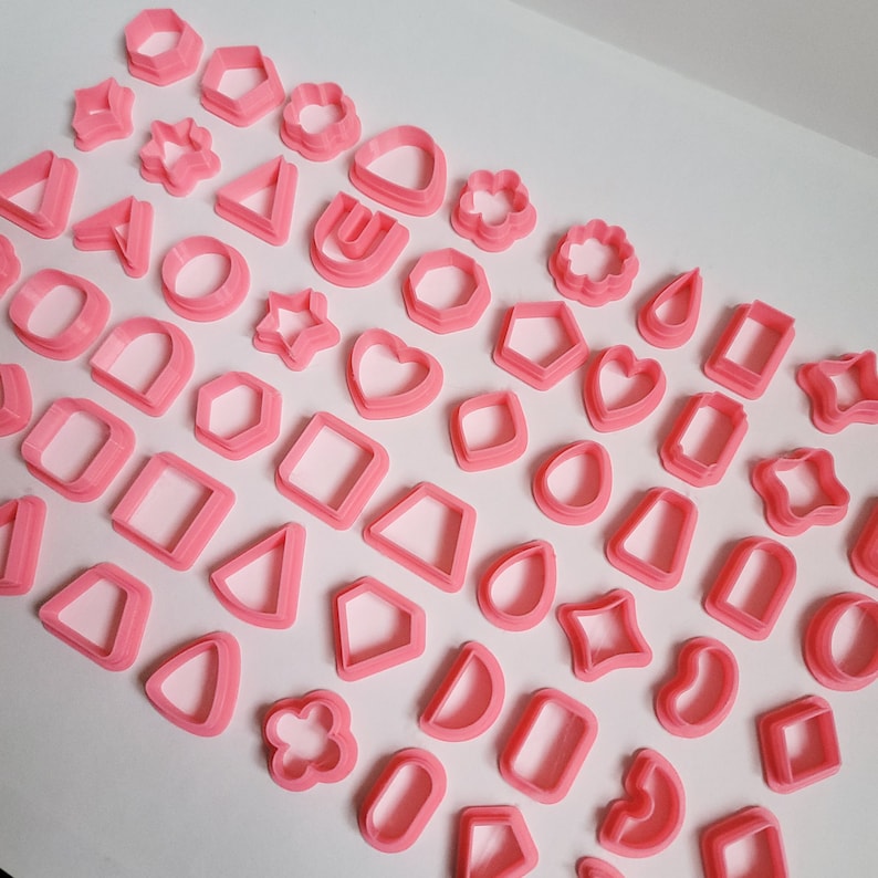 May include: A set of pink plastic cookie cutters in various shapes, including hearts, stars, circles, and geometric shapes.