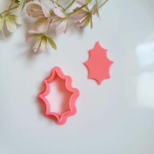May include: Two pink plastic cookie cutters shaped like a starburst. The cutters are on a white surface.