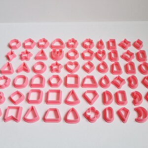 May include: A set of 48 pink plastic cookie cutters in various shapes, including stars, hearts, circles, squares, triangles, diamonds, and flowers.