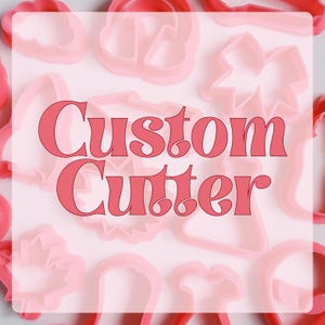 May include: A collection of pink plastic cookie cutters in various shapes, including stars, trees, and a bell. The text "Custom Cutter" is written in bold, red letters across the centre of the image.