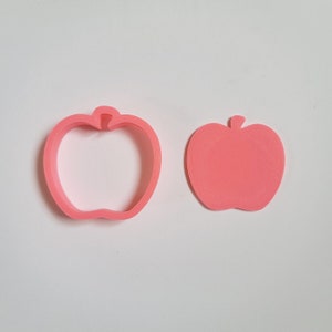 Könnte beinhalten: Zwei rosafarbene, plastikförmige Ausstecher in Apfelform. Einer ist eine feste Apfelform und der andere ist eine Umrandung eines Apfels.