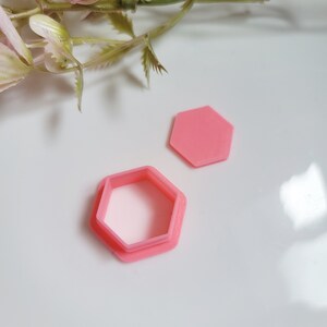 May include: Two pink plastic hexagon cookie cutters, one is a solid shape and the other is a ring-shaped cutter.