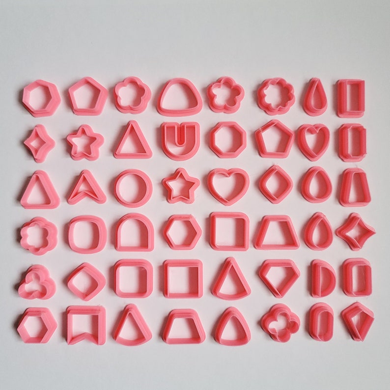 May include: A set of 48 pink plastic cookie cutters in various shapes, including stars, hearts, diamonds, circles, and geometric shapes.