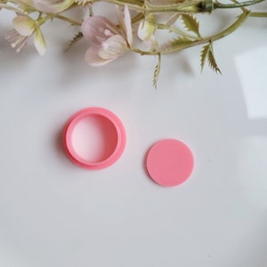 May include: A pink plastic mould for making round cakes or biscuits. The mould is in two pieces, a base and a top. The base is shown in the image.