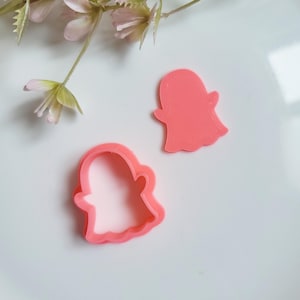 May include: Two pink plastic ghost cookie cutters. One is solid and the other is a cutout.