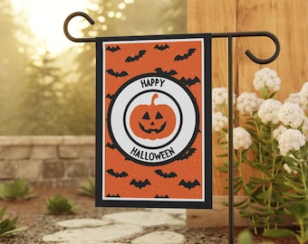 May include: A Halloween garden flag featuring a pumpkin design with the words "Happy Halloween." The flag has an orange background with black bats. The flag is displayed on a black metal stand in a garden setting.