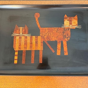 May include: A rectangular black serving tray featuring a decorative inlay of two cats crafted from various shades of brown wood veneer. The cats have stylized bodies, long whiskers, and distinct striped patterns, set against a glossy black background.