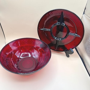May include: A set of two ruby red glass serving dishes. One is a round bowl, and the other is a divided serving plate with a black accent. Both have a textured pattern and are likely vintage.