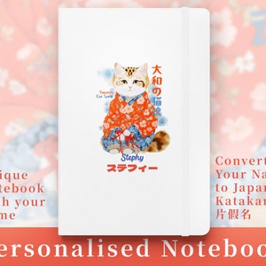 May include: A white notebook featuring a Japanese-style illustration of a cat wearing a kimono. The text "大和の猫魂" is written in Japanese characters on the notebook. The text "Stephy スラフィー" is also written on the notebook.
