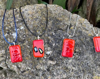 May include: Four rectangular red glass pendant necklaces with silver-tone bails. One pendant has a blue cord, one has a black cord, and two have silver chains. One pendant has two small, colorful glass accents.
