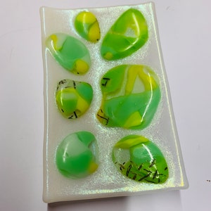 May include: A white rectangular dish with a iridescent finish features six green and yellow glass stones. The stones have a marbled effect and some have black lines.