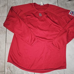 May include: Red long-sleeve baseball jersey with a white "World Series" patch on the right sleeve and a white "St. Louis Cardinals" logo on the front.