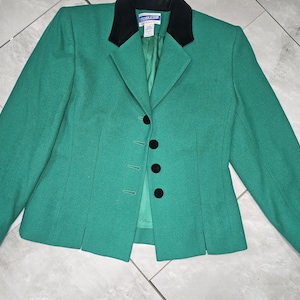 Könnte beinhalten: Ein grüner Blazer mit einem schwarzen Samtkragen und drei schwarzen Knöpfen. Der Blazer hat einen einreihigen Verschluss und lange Ärmel.