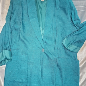 Könnte beinhalten: Ein blauer Blazer mit einem einzigen Knopfverschluss und zwei Taschen. Der Blazer hat ein Satin-Futter und einen Kragen.