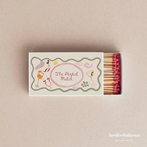 May include: A rectangular matchbox with a decorative border and the text "The Perfect Match" inside a pink oval. The box features illustrations of cocktails and food. The matches have pink tips.