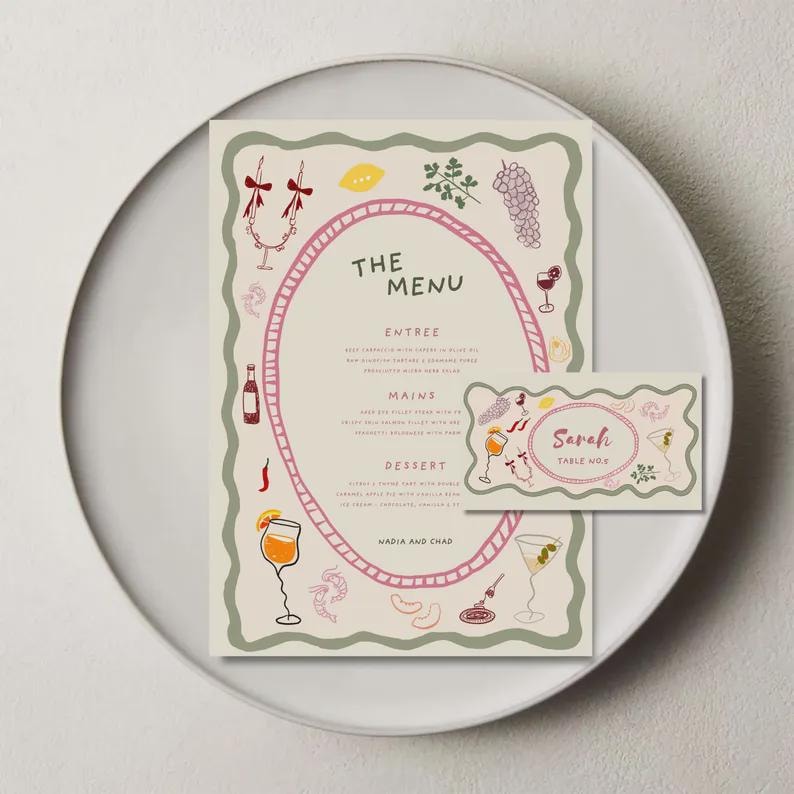 May include: A menu and place card set with a whimsical design. The menu features an oval frame with illustrations of food and drinks. The place card has the name "Sarah" and "Table No. 2". The set is on a white plate.