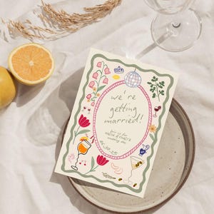 May include: A rectangular wedding invitation card featuring a wavy green border and a central pink oval frame. The text reads we're getting married! Join us for Nadia & Chad's wedding day 06.30.25. Illustrations include a disco ball, flowers, and cocktails.