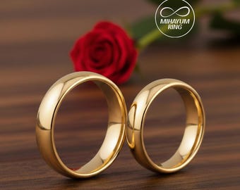 May include: Two gold wedding bands are displayed on a wooden surface, with a red rose in the background. The rings are smooth and shiny, reflecting the light. The rings are from Mihayum Ring.