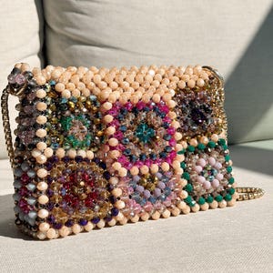 May include: A rectangular beaded handbag with a gold chain strap. The bag features a mosaic pattern of colorful beads in shades of pink, green, blue, and beige. The top of the bag is covered in beige beads.