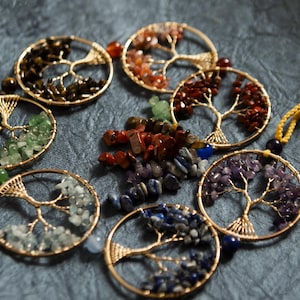 May include: Six gold wire tree of life ornaments with different colored gemstones. The ornaments are on a gray textured surface.