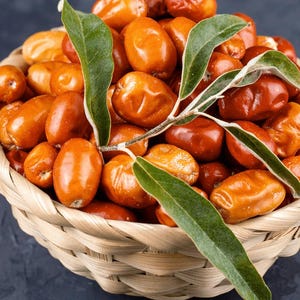 May include: A woven light-colored basket filled with numerous small, oval-shaped orange and reddish-brown fruits. A thin, light-colored stem with several elongated, pointed green leaves rests across the top of the pile of fresh, smooth-skinned fruits.