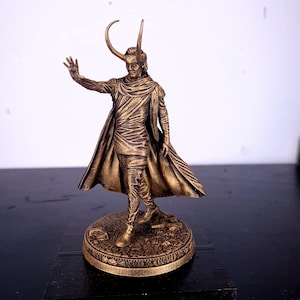 Op de afbeelding: Een gouden beeldje van een personage met hoorns, dat een lange robe draagt en op een ronde basis staat.
