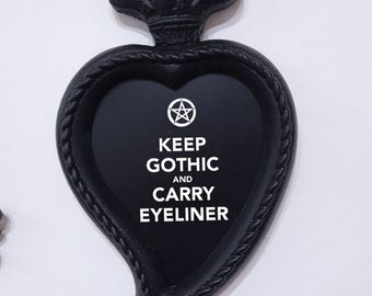 Pode incluir: Moldura preta em forma de coração com um pentagrama e o texto "Keep Gothic and Carry Eyeliner". A moldura está presa a um crânio preto com uma corrente dourada.
