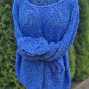 May include: A vibrant blue knit sweater displayed on a mannequin. The sweater has a round neckline and long sleeves, with the sleeves tied in front. The knitwear is a solid color, and the texture is visible.