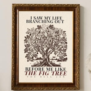 May include: A framed print with a brown wooden frame. The print features a sepia-toned illustration of a tree with the text "I SAW MY LIFE BRANCHING OUT" and "BEFORE ME LIKE THE FIG TREE THE BELL JAR". The print is displayed on a wooden surface.