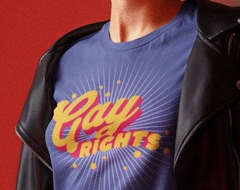 Puede incluir: Una camiseta azul marino con las palabras "Gay Rights" en amarillo y rosa, sobre un diseño de rayos de sol. La camiseta se combina con una falda vaquera y una chaqueta de cuero negra.