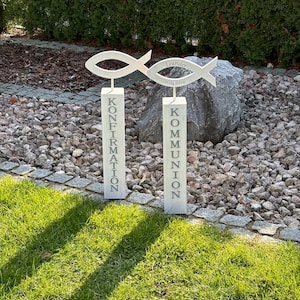 Könnte beinhalten: Zwei weiße Holzschilder mit den Worten "Konfirmation" und "Kommunion" darauf. Die Schilder sind mit einem Holzfischsymbol und dem Namen "Leander" sowie dem Datum "21.04.2024" verziert.