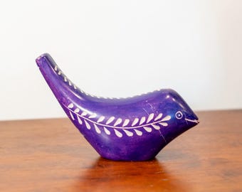 May include: A handcrafted, purple bird figurine with white leaf-like patterns. The sculpture has a curved shape and a small eye detail. This decorative item is likely made of stone or a similar material.