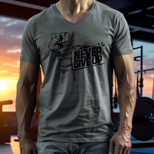 May include: Gray V-neck t-shirt with a black graphic of a clenched fist wrapped in bandages, and the words "NEVER GIVE UP" in bold, black letters. The shirt is made of a soft material.