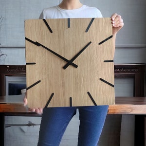 Może przedstawiać: Drewniany zegar z czarnymi wskazówkami i jasnym wykończeniem z drewna. Zegar jest trzymany przed ciałem osoby.