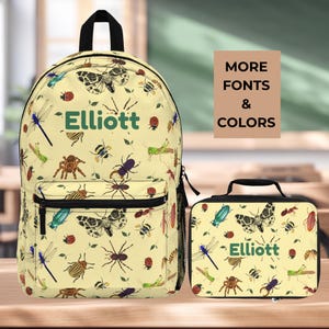 May include: A yellow backpack and matching lunch bag set. The backpack and lunch bag are covered in a pattern of colorful insects, including butterflies, spiders, and dragonflies. The name "Elliott" is printed in green on both items. The text "MORE FONTS & COLORS" is also visible.