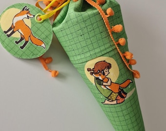 May include: A green fabric cone-shaped gift bag with a grid pattern, decorated with orange and yellow ribbons and pom-poms. The bag features illustrations of a fox and a girl with a fox. A round tag with a fox illustration is attached.