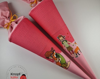 May include: Two pink fabric school cones with a girl and fox illustration. The cones have a grid pattern and a yellow ribbon tied at the top. The text "Knopf-käfer" is printed on one cone.