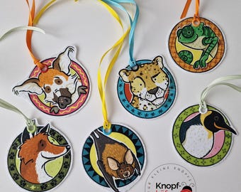 May include: Six colorful round tags with animal illustrations and a tag with the text "Kleine Knopf-Käfer" in German. The tags are attached to colorful ribbons.